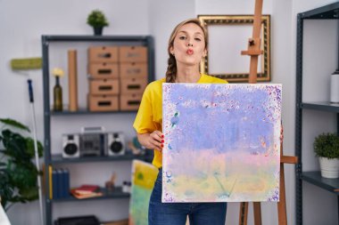 Kanvas tutan genç sarışın kadın kameraya bakıyor. Öpücük üflüyor. Sevimli ve seksi. aşk ifadesi. 