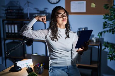 Genç Brezilyalı kadın geceleri dokunmatik ped kullanıyor ofiste çalışıyor güçlü biri kol kası gösteriyor, kendinden emin ve gururlu. 