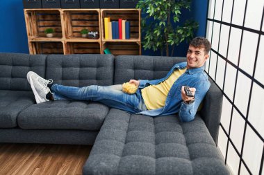 Evdeki kanepede uzanmış film izleyen İspanyol genç adam.