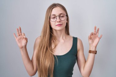 Young caucasian woman standing over white background relaxed and smiling with eyes closed doing meditation gesture with fingers. yoga concept. 