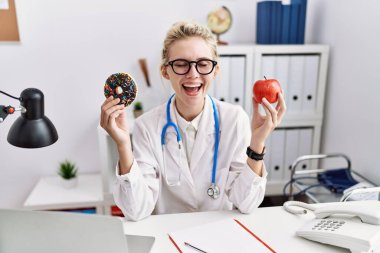 Klinikte elinde kırmızı elmayla donut tutan genç bir doktor. Gülmekten çatlıyor.. 
