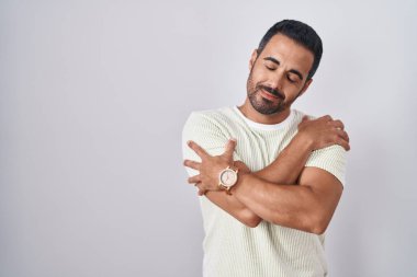 Soyutlanmış arka planda sakallı İspanyol bir adam kendine sarılıyor mutlu ve pozitif, kendinden emin gülümsüyor. Sevgi ve özgüven. 