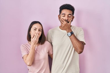 Young hispanic couple together over pink background bored yawning tired covering mouth with hand. restless and sleepiness. 