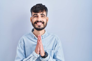 Mavi arka planda sakallı genç bir İspanyol. Elleriyle birlikte dua ediyor. Affedilmek için dua ediyor.. 