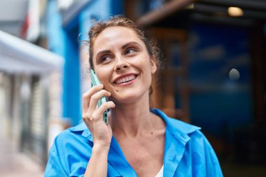 Gülümseyen genç bir kadın caddedeki akıllı telefondan konuşuyor.