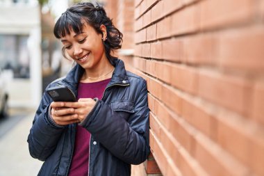 Genç, güzel, İspanyol bir kadın sokakta akıllı telefon kullanarak gülümsüyor.