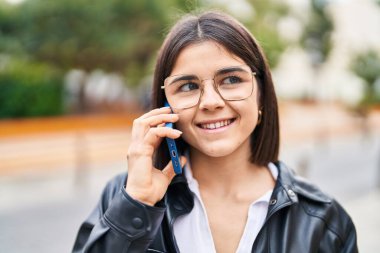 Genç, güzel, İspanyol bir kadın gülümsüyor ve caddede akıllı telefondan konuşuyor.