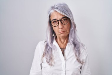 Beyaz arka planda duran gözlüklü orta yaşlı bir kadın depresif ve endişeli, sinirli ve korkmuş bir şekilde ağlıyor. hüzünlü ifade. 