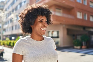 Afro-Amerikalı kadın gülümsüyor. Kendinden emin bir şekilde caddeye bakıyor.