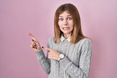 Pembe arka planda duran güzel bir kadın iki eliyle endişeli ve gergin, endişeli ve şaşırmış ifadesini işaret ediyor. 