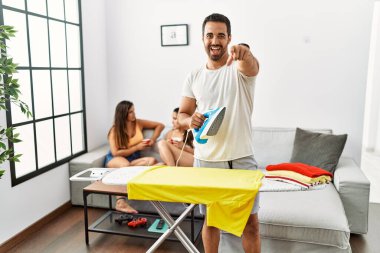 Genç İspanyol ütülü adam evde seni ve kamerayı işaret ediyor, pozitif ve neşeli gülümsüyor. 