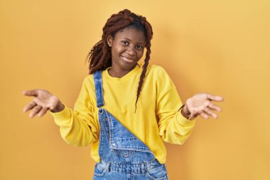 African woman standing over yellow background smiling cheerful offering hands giving assistance and acceptance. 