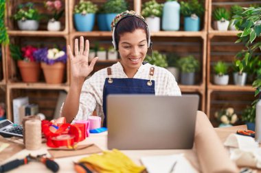 Çiçekçide çalışan genç İspanyol kadın video çekiyor. Pozitif görünüyor ve gülümsüyor. Kendine güvenen bir gülümsemeyle dişlerini gösteriyor. 
