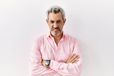 Orta yaşlı İspanyol bir adam soyutlanmış arka planda duruyor şüpheci ve gergin, yüzünde çapraz kollarla onaylamayan bir ifade. negatif kişi. 