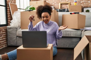 Young african american woman showing keys of new home on video call celebrating achievement with happy smile and winner expression with raised hand 