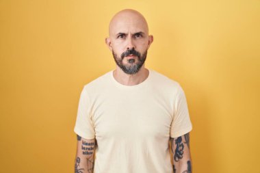 Sarı arka planda duran İspanyol dövmeli adam yüzünde ciddi bir ifadeyle rahatladı. Basit ve doğal bir şekilde kameraya bakıyorsun.. 