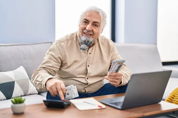 Hombre Pelo Gris Mediana Edad Usando Portátil Contando Dólares Casa —  Fotos de Stock