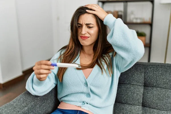 Young woman looking pregnancy test result sitting on sofa at home