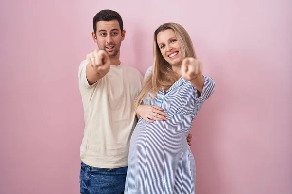 Casal Jovem Esperando Bebê Sobre Fundo Rosa Apontando Para Você — Fotografia de Stock