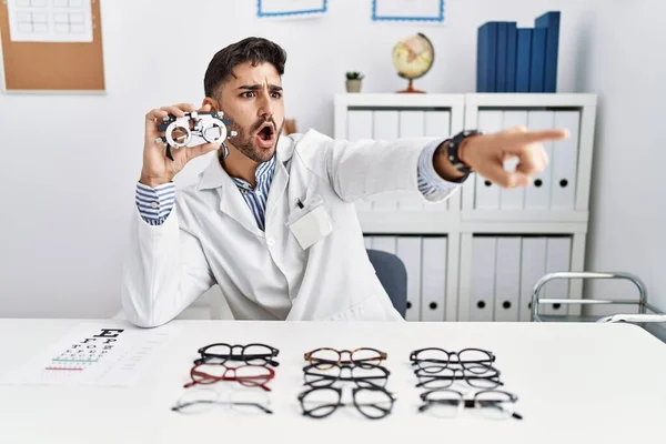 Young Optician Man Holding Optometry Glasses Pointing Finger Surprised Ahead — 图库照片