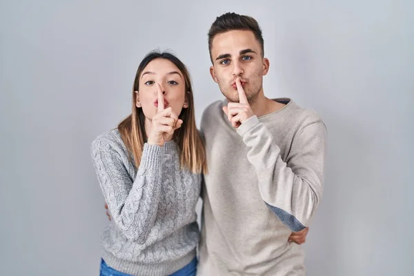 Young Hispanic Couple Standing White Background Asking Quiet Finger Lips — Stockfoto