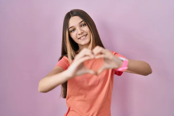 手でハートのシンボルの形をする愛のピンクの背景に笑みを浮かべて立って10代の女の子 ロマンチックなコンセプト — ストック写真