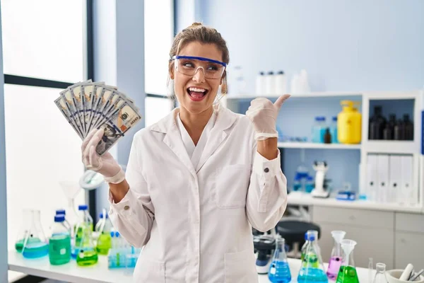 Young Woman Working Scientist Laboratory Holding Money Pointing Thumb Side — Stock Photo, Image