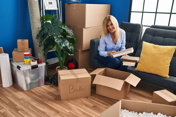 Middle Age Blonde Woman Smiling Confident Unpacking Books Package Home — Stockfoto