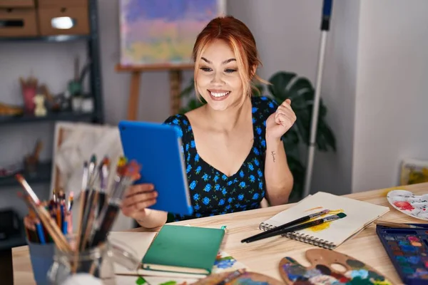 年轻的高加索女人坐在艺术工作室里用平板电脑做视频通话 自豪地尖叫着 高举双臂庆祝胜利和成功 — 图库照片