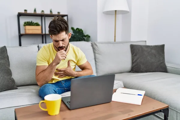 Young man with beard using laptop at home feeling unwell and coughing as symptom for cold or bronchitis. health care concept.