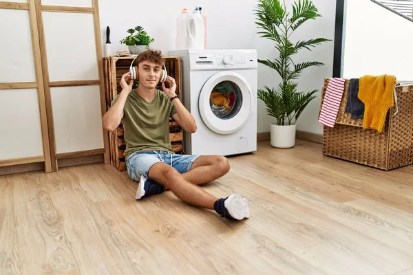 Young Caucasian Man Listening Music Waiting Washing Machine Laundry Room — Zdjęcie stockowe