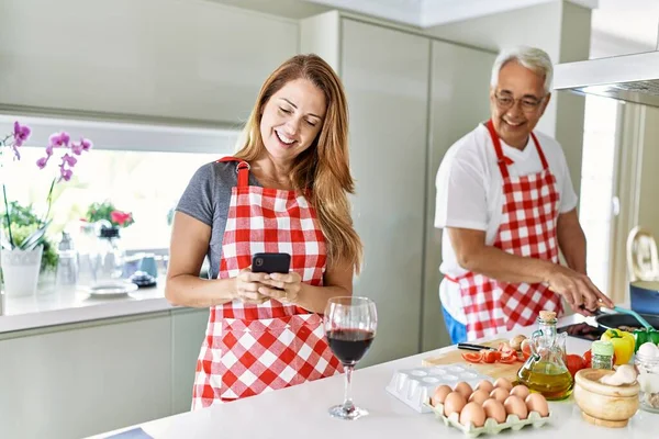 Μεσήλικες Ζευγάρι Ισπανόφωνων Χαμογελά Ευτυχισμένη Μαγειρική Και Χρήση Smartphone Στην — Φωτογραφία Αρχείου