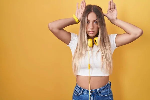 Young Blonde Woman Standing Yellow Background Wearing Headphones Doing Bunny — Foto Stock