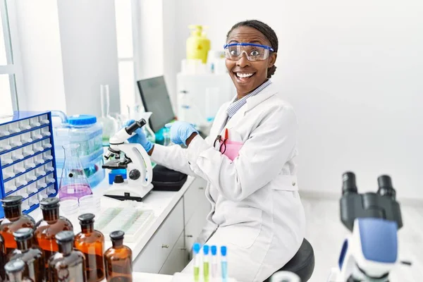 African woman working at scientist laboratory smiling happy pointing with hand and finger