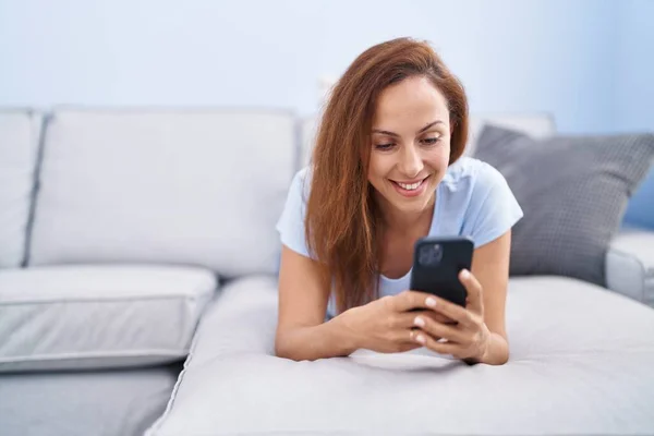 使用智能手机躺在沙发上在家里的年轻女人 — 图库照片