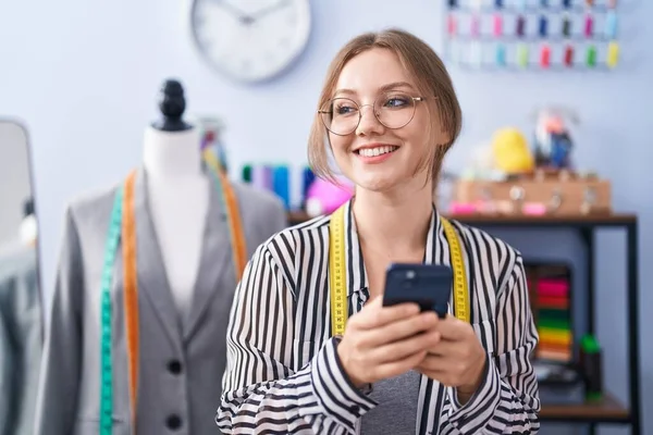 在裁缝店用智能手机自信地微笑着的金发女裁缝 — 图库照片