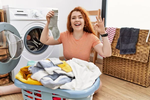 若い赤毛の女性は手と指でOkサインを行う肯定的な笑顔洗濯機に汚れた洗濯機を入れて 成功した表現 — ストック写真