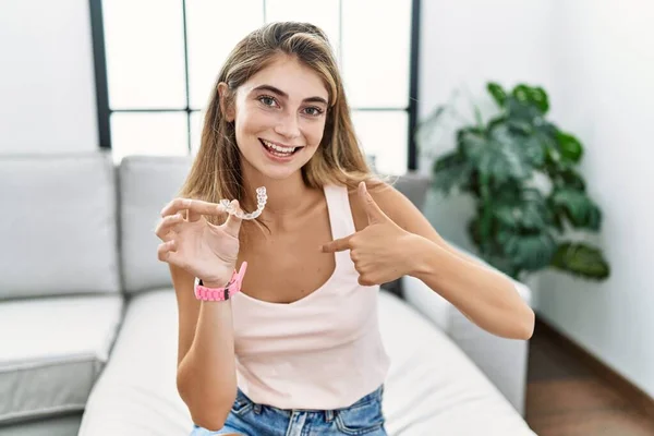 Young blonde woman holding invisible aligner orthodontic looking confident with smile on face, pointing oneself with fingers proud and happy.