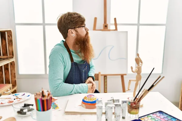 红头发的男人 留着长胡子 在艺术工作室里画着黏土碗 朝旁边看 带着自信的微笑放松自己的姿态 — 图库照片