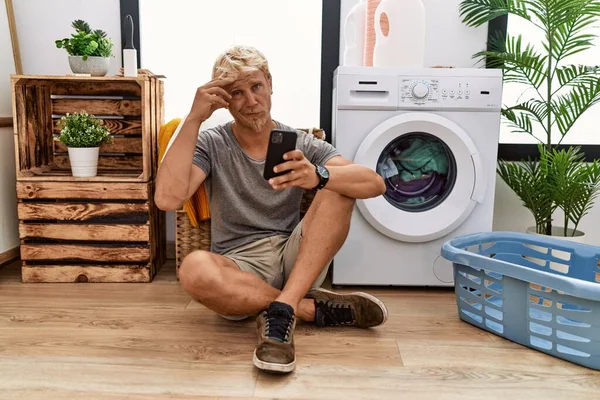 Genç Sarışın Adam Çamaşır Yıkıyor Akıllı Telefon Kullanıyor Alnındaki Sorun — Stok fotoğraf