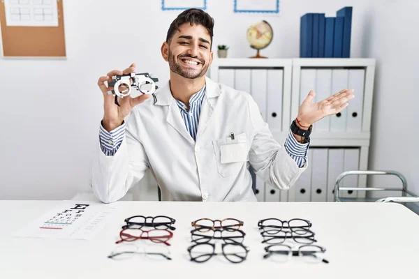 Young Optician Man Holding Optometry Glasses Pointing Aside Hands Open — Fotografia de Stock