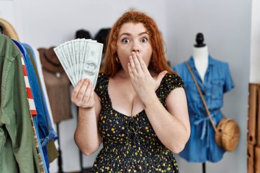 Alışveriş torbaları tutan genç, kızıl saçlı bir kadın ve ağzıyla dolar örten bir kadın. Şok olmuş ve hata yapmaktan korkuyor. şaşırmış ifade 