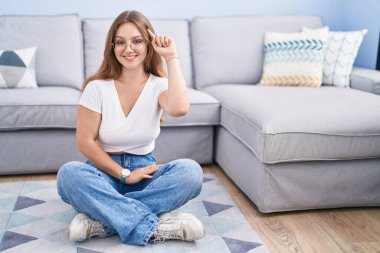 Oturma odasında yerde oturan beyaz bir kadın tek parmakla işaret ederek gülümsüyor, harika bir fikir ya da düşünce, iyi bir hafıza. 