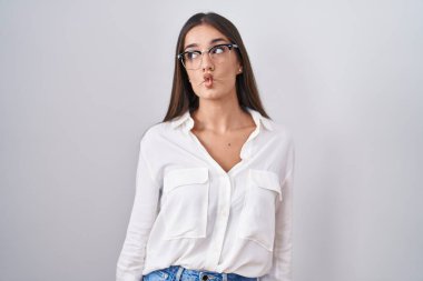 Young brunette woman wearing glasses making fish face with lips, crazy and comical gesture. funny expression. 