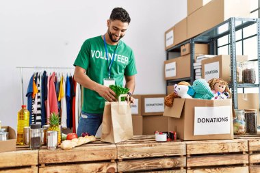 Gönüllü üniformalı genç bir Arap, hayır kurumunda alışveriş poşeti hazırlıyor.