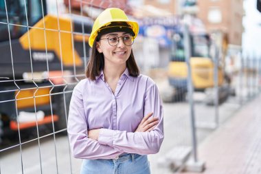 Young hispanic woman architect standing with arms crossed gesture at street