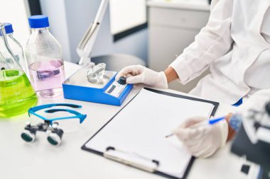 Young hispanic woman scientist weighing diamond writing report at laboratory