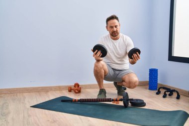 Genç beyaz adam gülümsüyor. Spor merkezinde spor yapmak için barlara ve disklere hazırlanıyor.