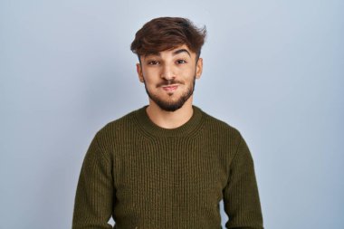 Arab man with beard standing over blue background puffing cheeks with funny face. mouth inflated with air, crazy expression. 