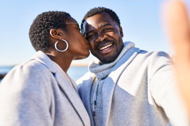 Erkek ve kadın bir arada, deniz kenarında selfie çekiyorlar.